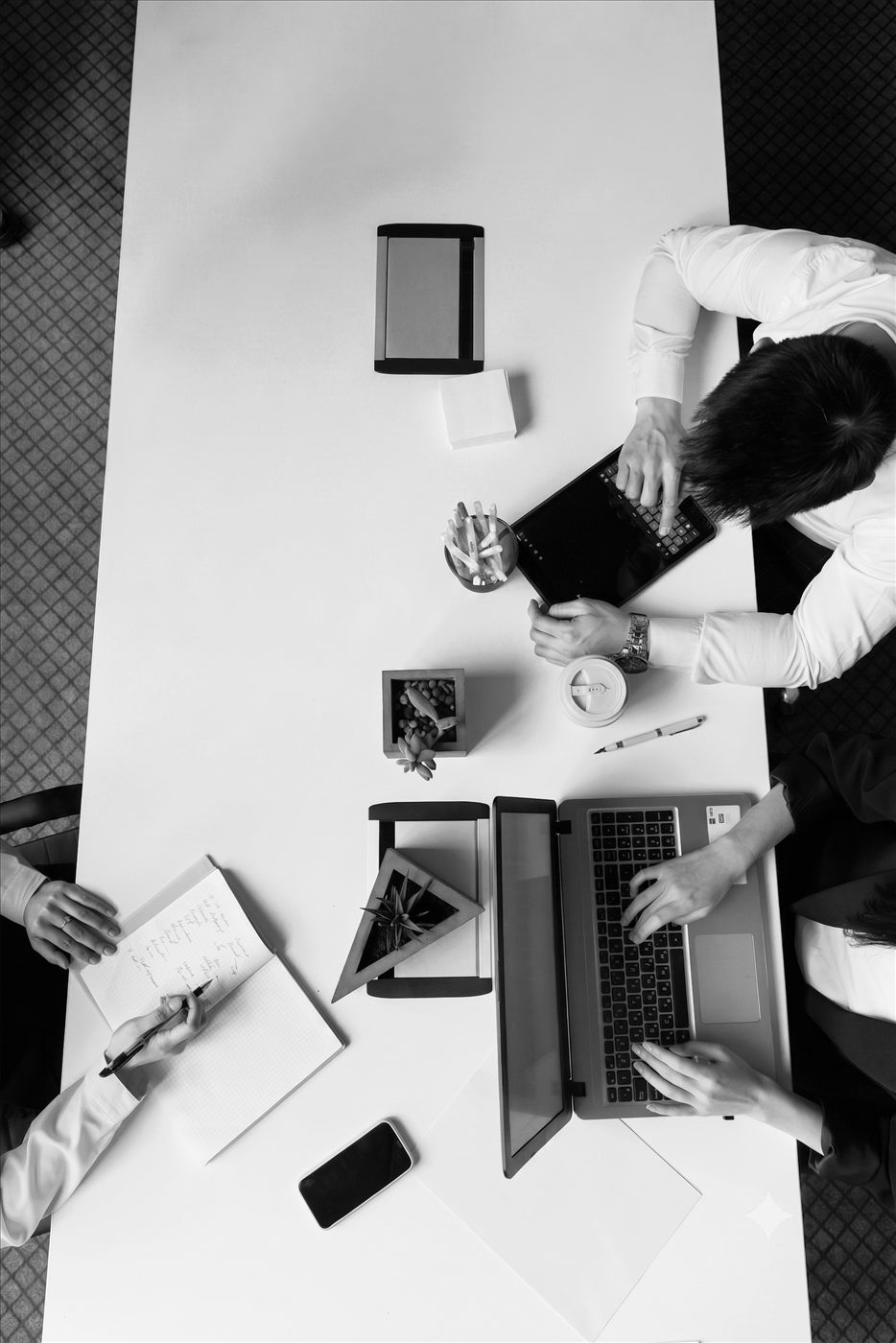 Vista de cima de uma mesa de trabalho com notebooks e pessoas em reunião